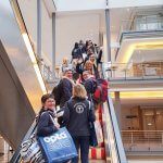 Kolleginnen auf Rolltreppe mit Gepäck und Firmenkleidung
